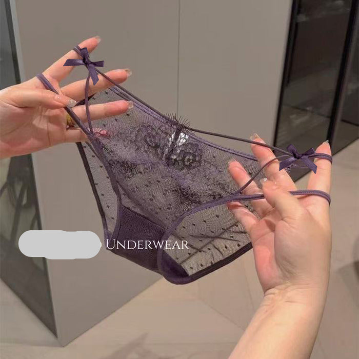 A pair of sheer purple lace thong underwear with small bow details on the side straps, held up by two hands against an indoor background. 