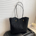 A black leopard-print tote bag with thin shoulder straps and small gold hardware, resting on a black leather chair in front of white horizontal blinds. A book and a white mug are partially visible on the right side.