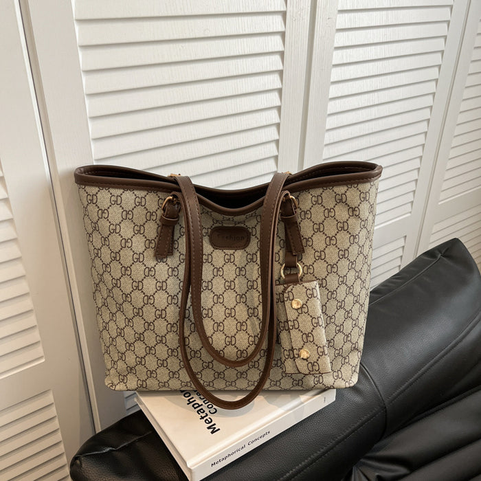 A Gucci tote bag in the classic GG Supreme canvas, featuring a beige and brown monogram pattern with dark brown leather handles and trim, resting on a white book on a black leather sofa in front of white louvered doors.