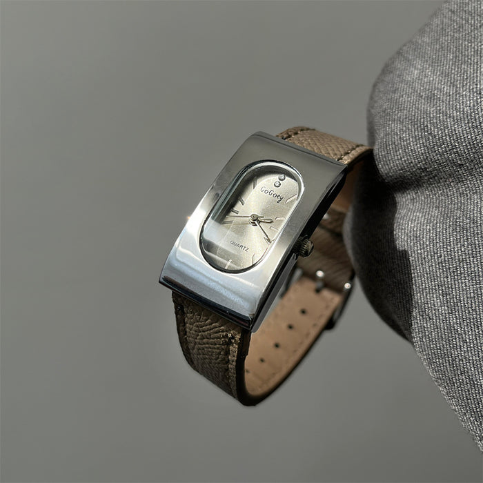 Vintage-style wristwatch with brown leather strap held by a gloved hand against a gray background