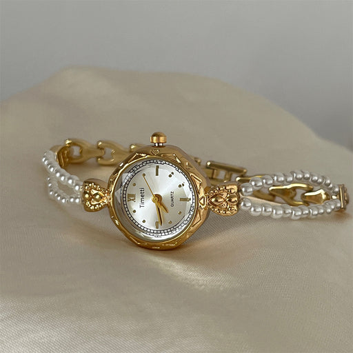 Gold wristwatch with pearl bracelet on a beige fabric background