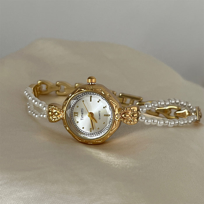 Gold wristwatch with pearl bracelet on a beige fabric background