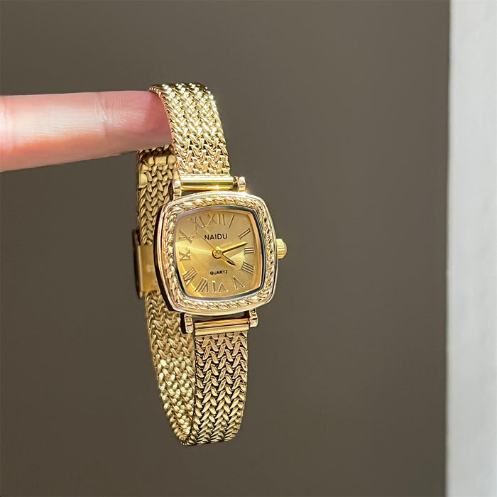 Gold wristwatch held by a finger against a gray background