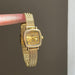 Gold wristwatch held by a finger against a gray background