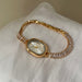 A gold-tone women's watch with a bezel-encased oval face and a link bracelet covered in clear rectangular crystals, resting on a white textured fabric surface.