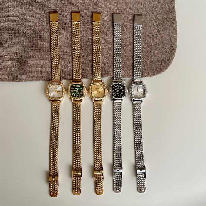 Four vintage-style wristwatches with mesh metal straps are arranged vertically on a light surface with a brown fabric prop behind them. The watches have gold-tone and silver-tone cases and straps, with one green dial and two white dials.