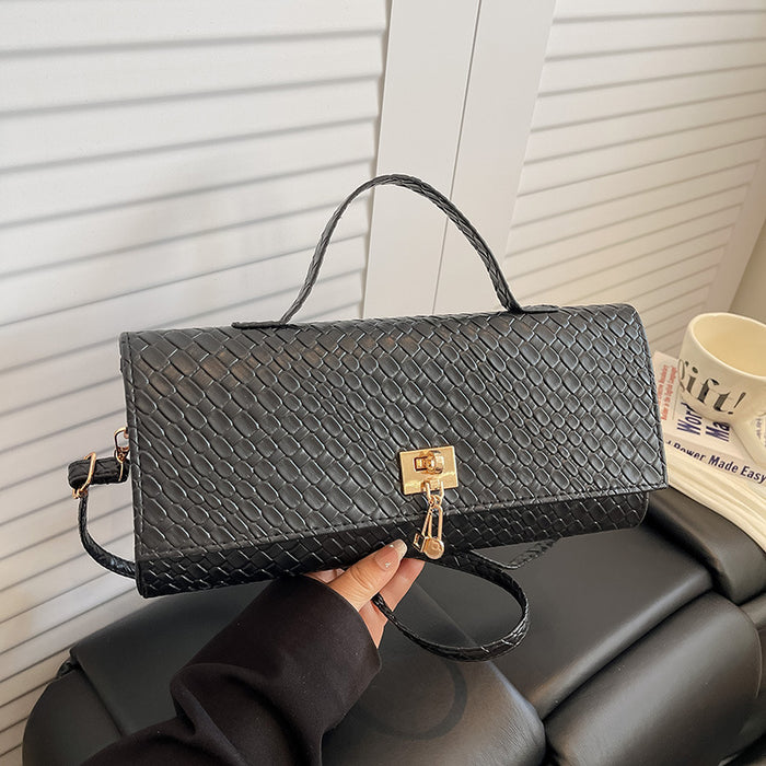 A black woven leather handbag with a top handle and gold-tone clasp, held by a hand in front of a white slatted door and black leather chair.