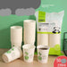 A bulk pack of disposable paper cups with several stacks and individual cups displayed. The cups are white with green leaf graphics and text.