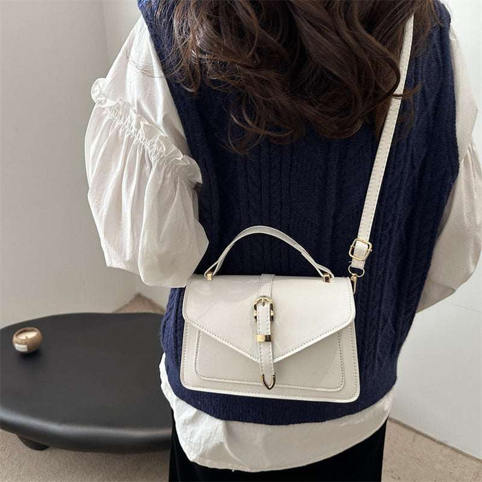 A person shown from the back wearing a navy cable-knit vest over a white blouse, carrying a small white top-handle handbag with a gold-tone clasp and shoulder strap.