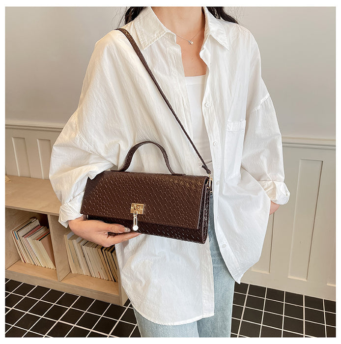 A person wearing an oversized white button-up shirt and light blue jeans carries a dark brown crocodile-embossed handbag with a top handle and shoulder strap in an indoor room with bookshelves.