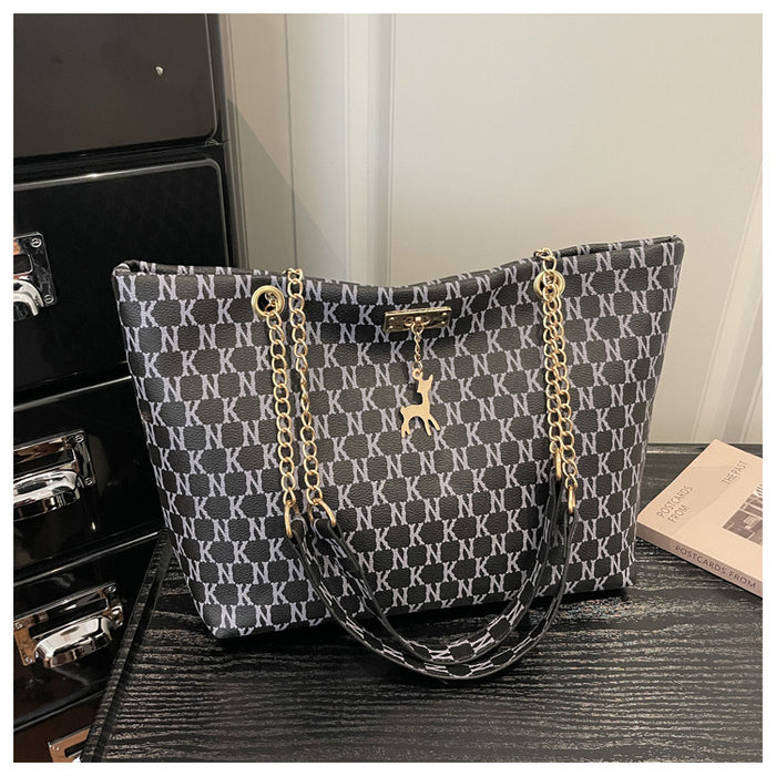 A tote bag with a black and white geometric monogram pattern, featuring gold-tone chain straps and a deer charm, displayed on a dark textured surface.