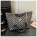 A tote bag with a black and white geometric monogram pattern, featuring gold-tone chain straps and a deer charm, displayed on a dark textured surface.
