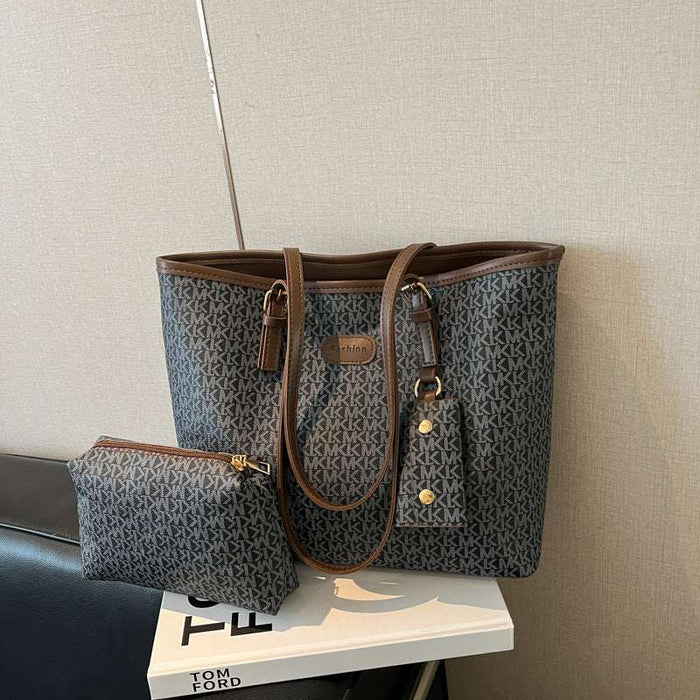 A dark gray and brown monogram tote bag with matching zip pouch, displayed on a white book against a beige textured wall.
