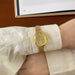 Gold wristwatch on a person's wrist with a white shirt sleeve.