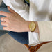 Hand wearing a gold watch with a neutral background