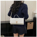 A woman shown from the back wearing a navy ribbed sweater and matching polka-dot pleated skirt, carrying a white textured top-handle handbag with a gold clasp over her shoulder in an indoor room setting.