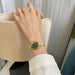 Hand wearing a gold watch with a neutral background