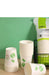 White paper cups with green leaf graphics, shown stacked and standing alongside a branded package on a tabletop against a green wall.