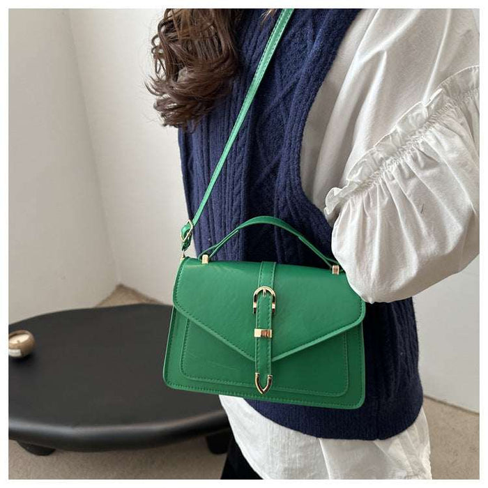 A woman wearing a navy blue cable-knit vest over a white puff-sleeve blouse carries a bright green leather shoulder bag with a top handle and gold-tone hardware.