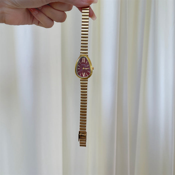 Gold wristwatch held by a hand against a white curtain background