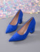 A pair of royal blue suede pointed-toe pumps with block heels, displayed on a gray surface with a sparkling multicolor sequin backdrop.