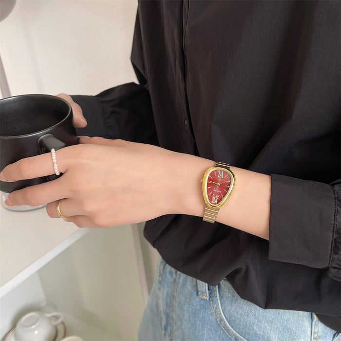 A close-up of a person wearing a gold-tone mesh watch with a red rose dial, holding a black mug while wearing a black shirt and light blue jeans.