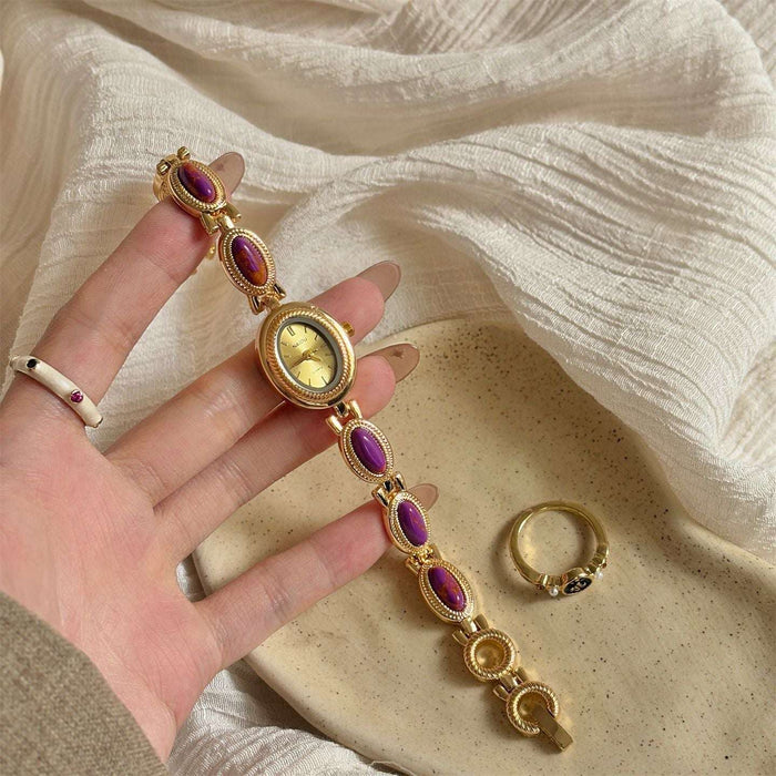 Gold bracelet with purple stones held by a hand on a textured beige surface.