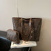 A brown Fendi tote bag with the signature FF monogram pattern and a matching zip pouch, displayed on a white book on a black leather chair against a beige wall.