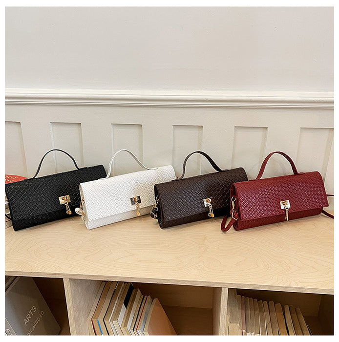 Four woven handbags in black, white, dark brown, and burgundy red are lined up on a light wood shelf against a white paneled wall.