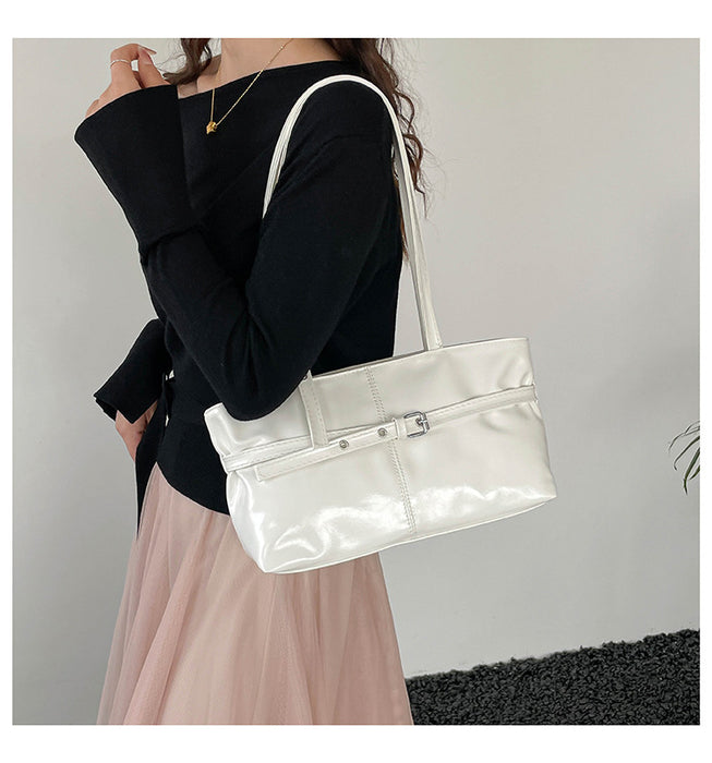 A woman wearing a black long-sleeve top and a light pink skirt carries a large glossy white shoulder tote bag with silver hardware against a plain light gray wall.