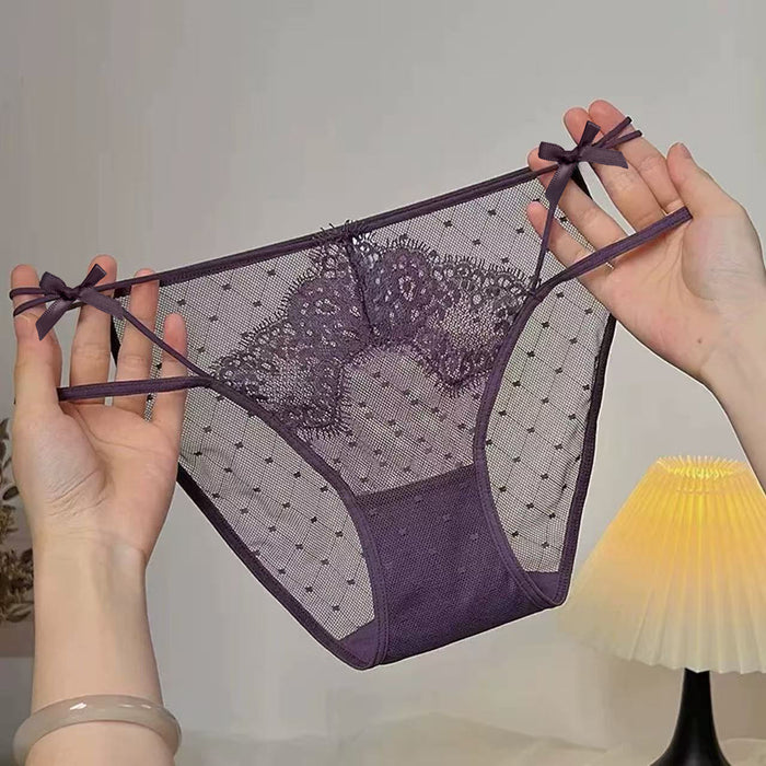 A pair of sheer purple lace and mesh panties with bow details on the sides, held up by two hands against a softly lit indoor background.