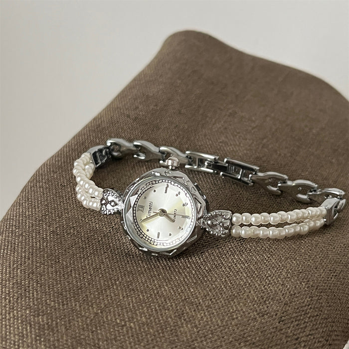 Silver watch with pearl bracelet on a brown surface
