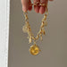 Gold charm bracelet with a watch charm held by a hand against a neutral background