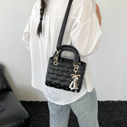A person wearing a white blouse and light blue jeans carries a black quilted Lady Dior-style handbag with gold hardware and a pearl charm, shown from the back in an indoor setting.