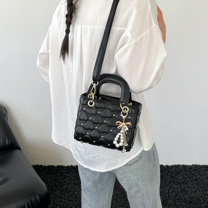 A person wearing a white blouse and light blue jeans carries a black quilted Lady Dior-style handbag with gold hardware and a pearl charm, shown from the back in an indoor setting.