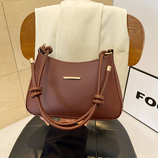 A brown leather handbag with knotted leather handles and gold-tone hardware, displayed on a black chair in front of a white draped fabric backdrop.