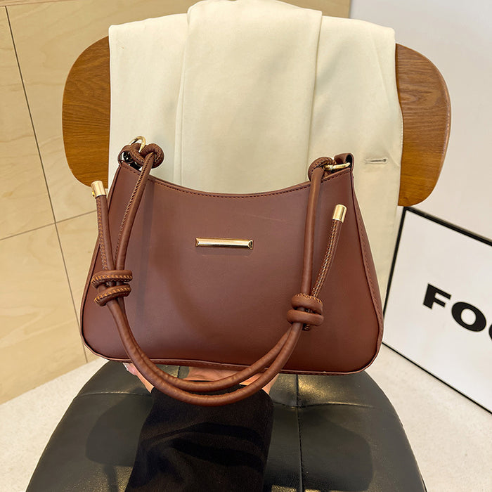 A brown leather handbag with knotted leather handles and gold-tone hardware, displayed on a black chair in front of a white draped fabric backdrop.