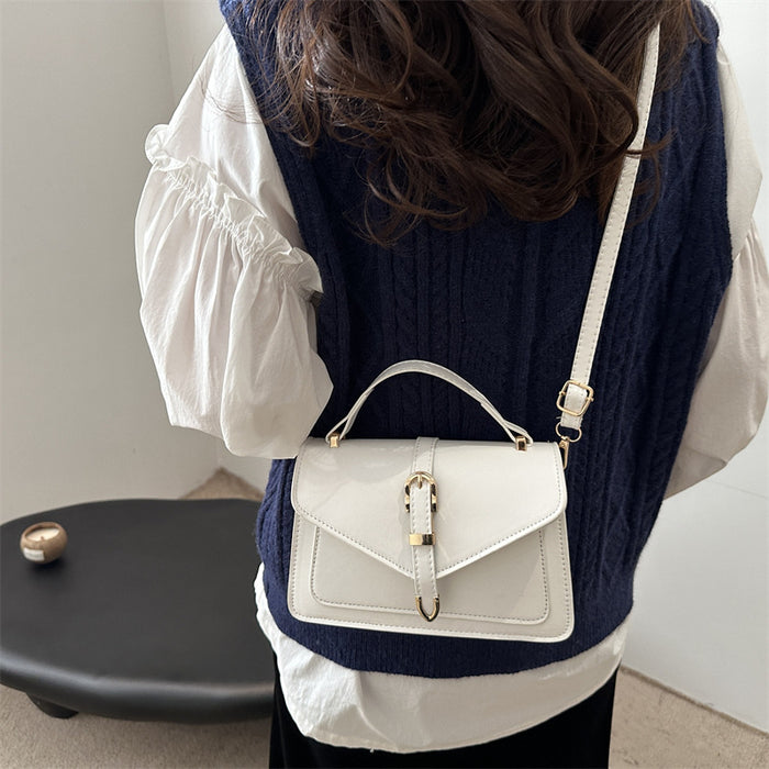 A person shown from the back wearing a navy cable-knit vest over a white blouse, carrying a small white top-handle handbag with a gold-tone clasp and shoulder strap.