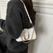 A person wearing a dark gray ribbed sweater carries a small white shoulder bag with a gold-tone chain strap and gold hardware against a white paneled wall.