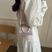 A person wearing a white blouse and white skirt carries a small pink glittery shoulder bag with a pearl bead handle in an indoor setting.