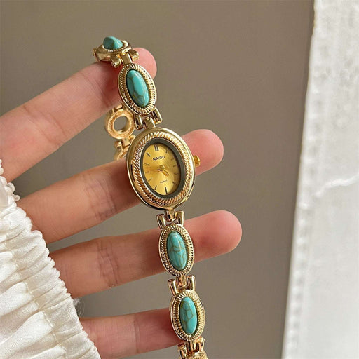 Gold watch with turquoise stones held by a hand against a neutral background