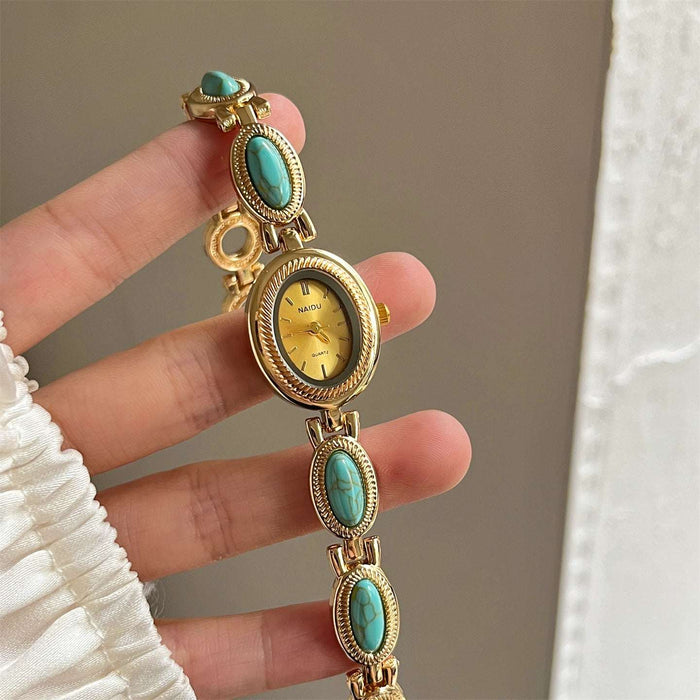 Gold watch with turquoise stones held by a hand against a neutral background