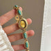 Gold watch with turquoise stones held by a hand against a neutral background