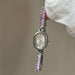 Silver watch with pink gemstone bracelet held by a hand against a neutral background