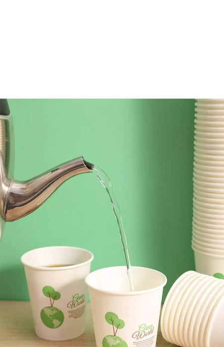 White paper cups with green apple graphics shown with a metal kettle pouring hot water into them, set against a light green background with stacked cups on the right.