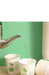 White paper cups with green apple graphics shown with a metal kettle pouring hot water into them, set against a light green background with stacked cups on the right.