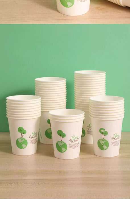 A set of white paper coffee cups with green globe and tree graphics, stacked in four piles on a light wood surface against a solid green background.