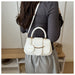 A woman wearing a dark gray ribbed long-sleeve top and light gray skirt carries a white faux-leather handbag with a top handle, white shoulder strap, gold-tone chain detail, and a round white charm labeled 'FASHION'.