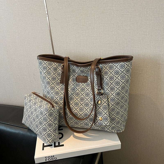 A tote bag with a brown leather trim and a matching zip pouch, both featuring a beige and blue geometric monogram pattern, displayed on a white book.