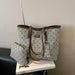 A tote bag with a brown leather trim and a matching zip pouch, both featuring a beige and blue geometric monogram pattern, displayed on a white book.